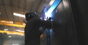 A technician welding, wielding a blue flame.